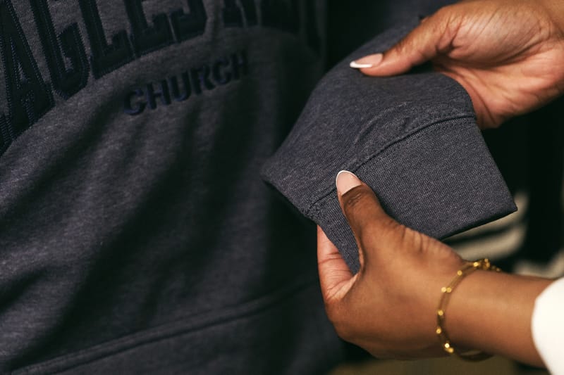 Hands inspecting the stitched cuff of a gray embroidered sweatshirt